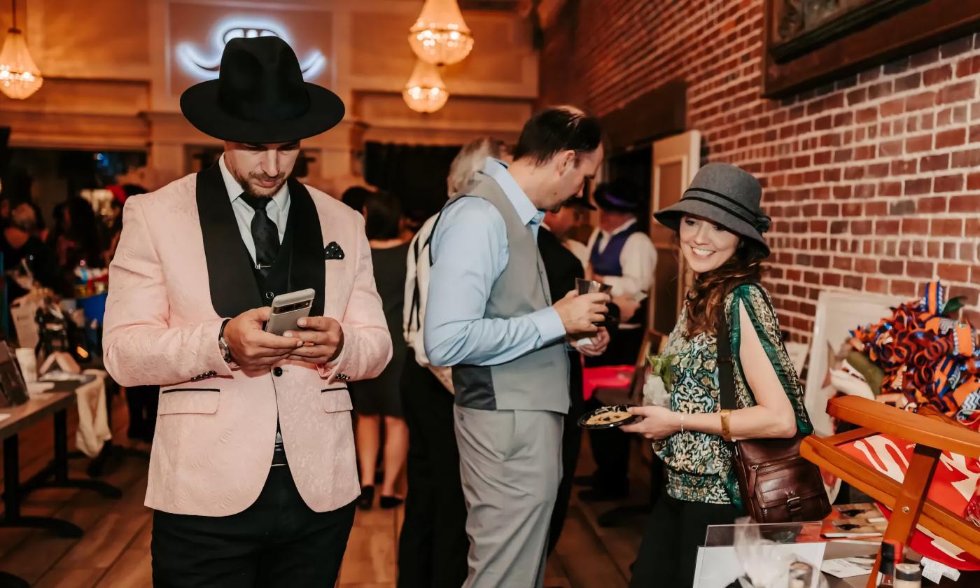 Guests in 1920's clothing check out the auction items at Prohibition Kitchen's Speakeasy for a Cure