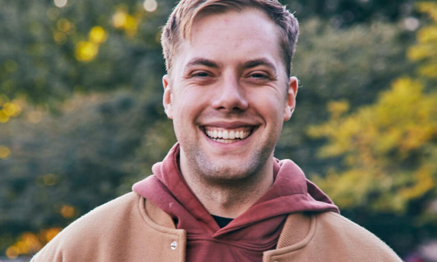 Bo Johnson smiles and poses in brown outwear with a matching shirt. 