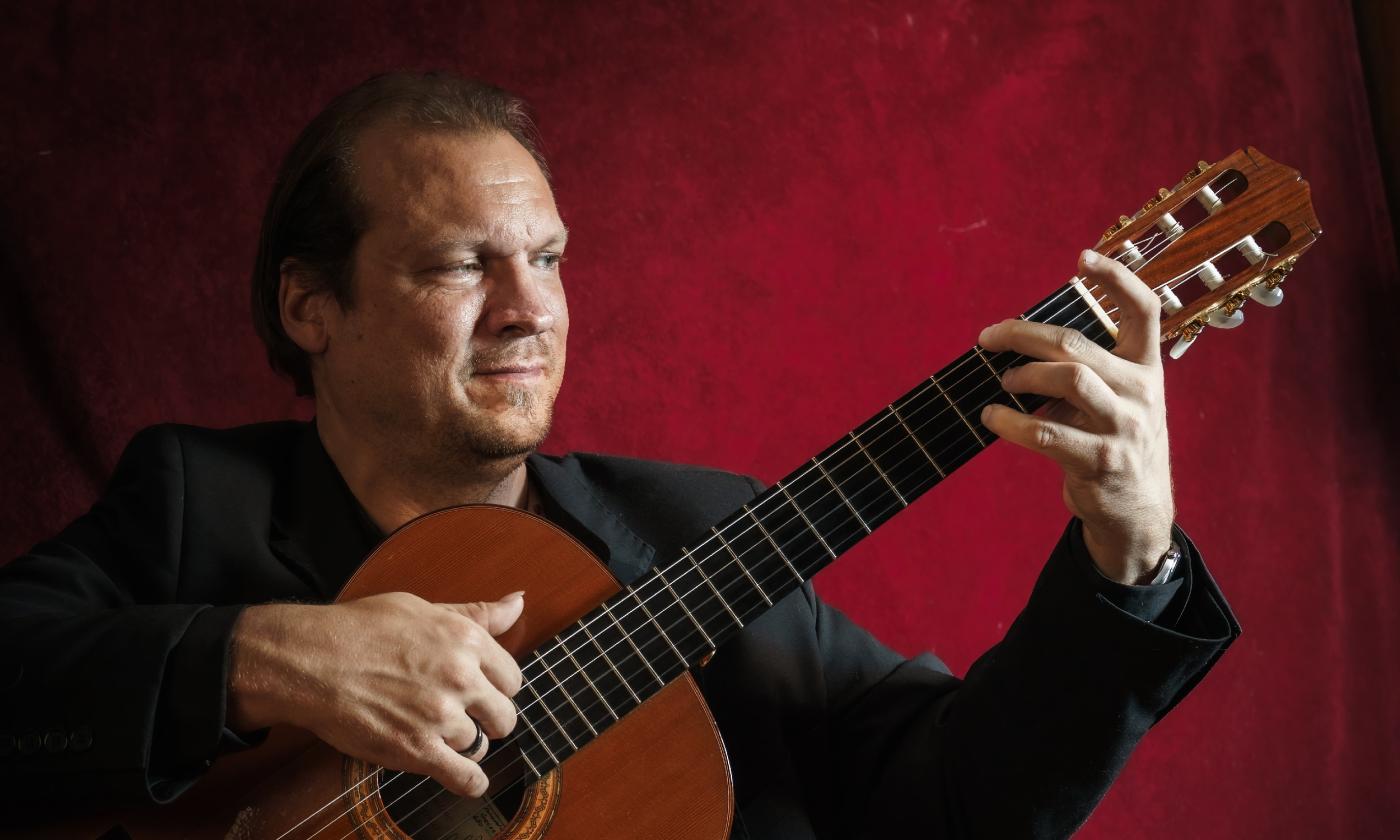 Guitarist Jonathan Dotson, with guitar, on stage, with a red background