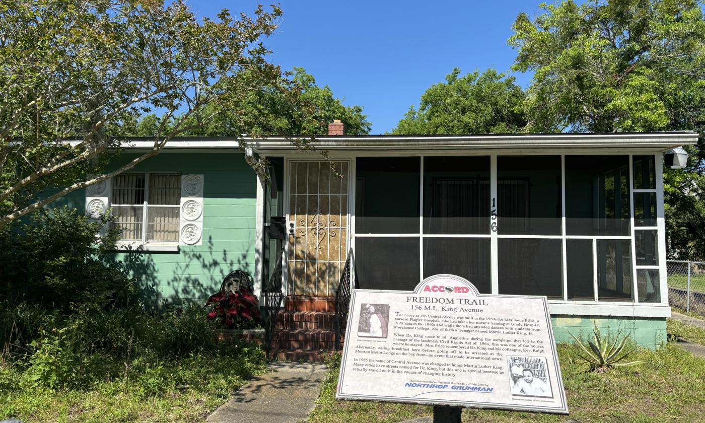 Green one-story cement block home with white details and screen porch. In the foreground, the 156 MLK ACCORD Freedom Trail Marker.