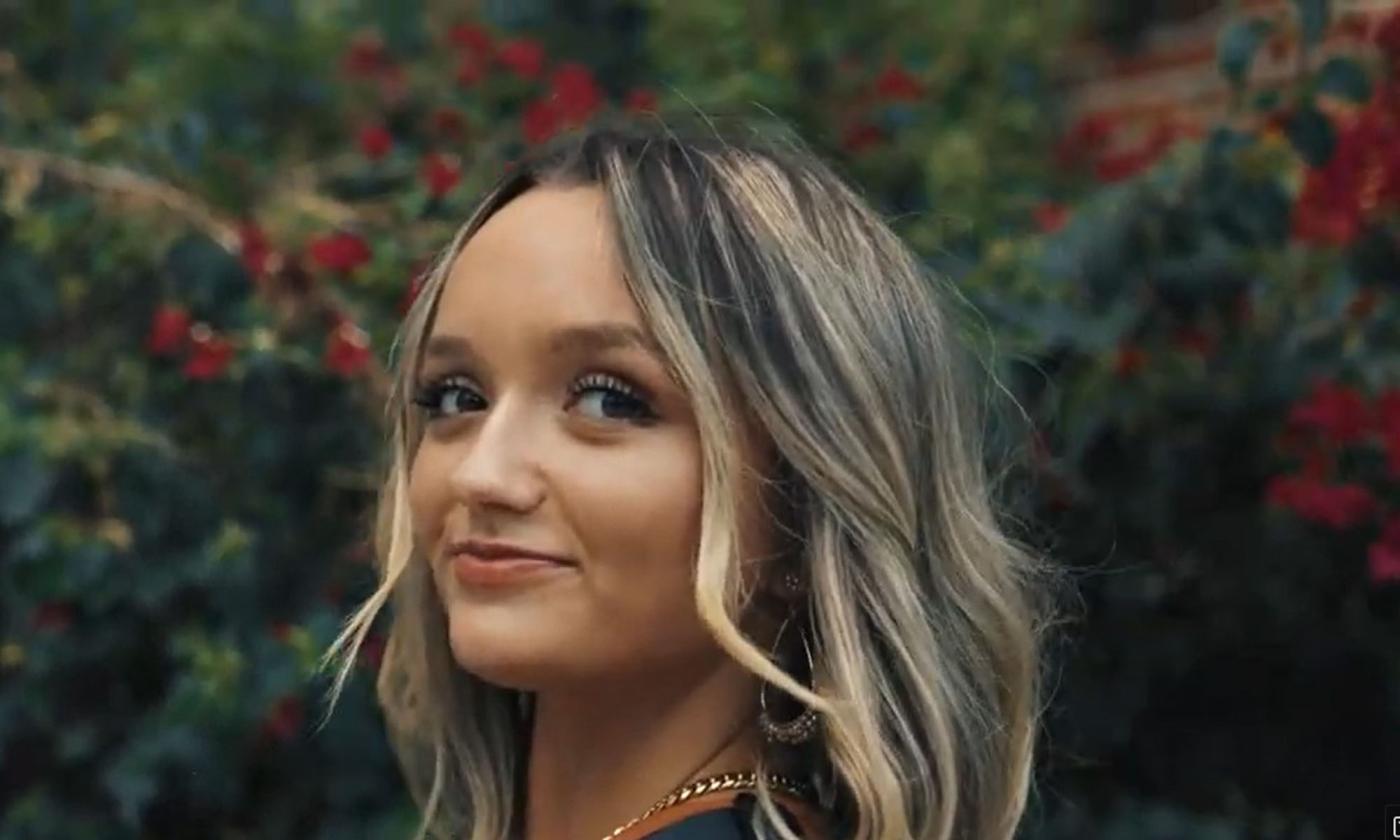 Country musician Aris Smith head shot, in front of hedge, smiling.