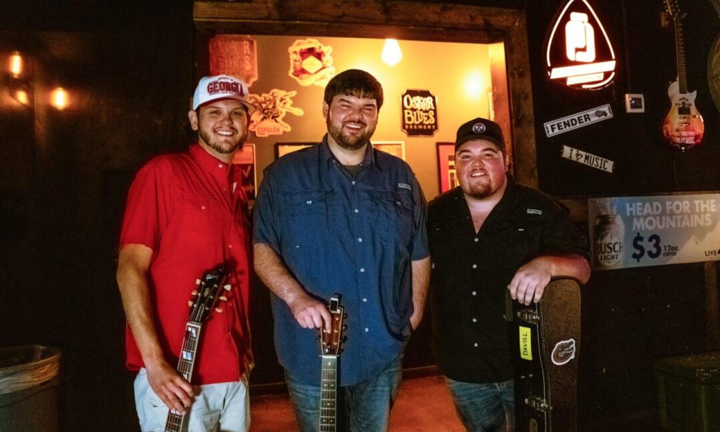 Davis Loose, Ethan Philips, and Justin Dukes smile and pose with their musical instruments. 