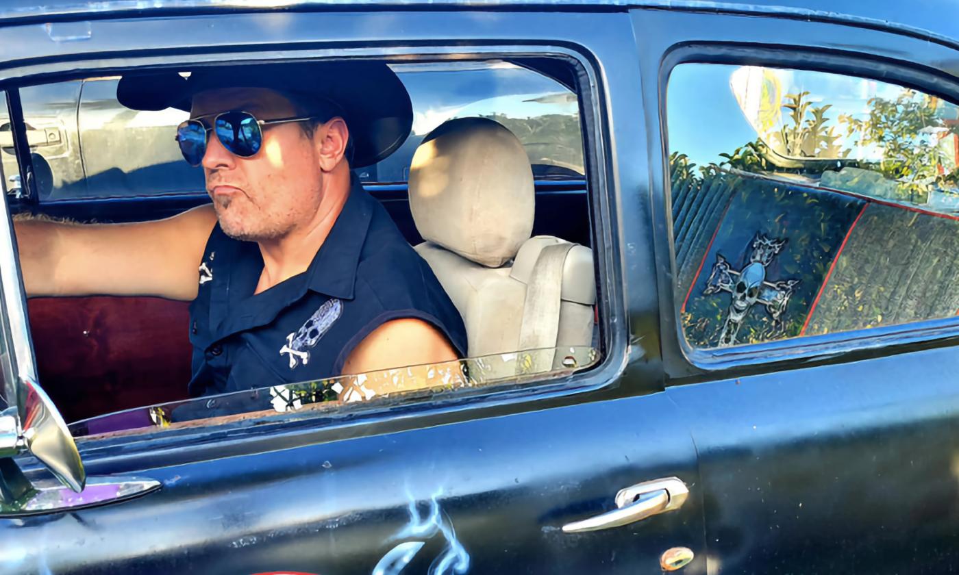 Marshal Horn posing in his classic automobile in sunglasses and a cowboy hat