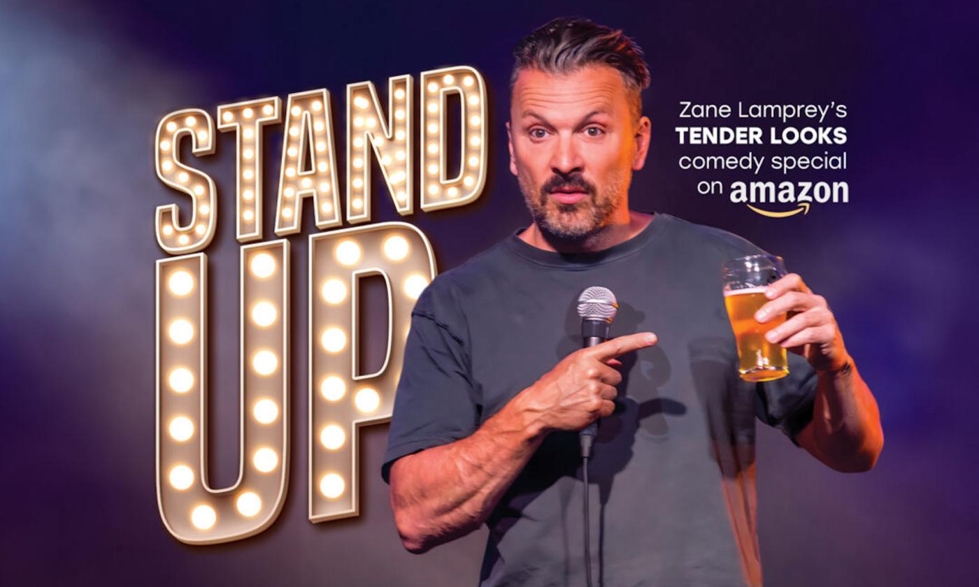 Comedian Zane Lamprey poses on stage with a drink in his hand. 