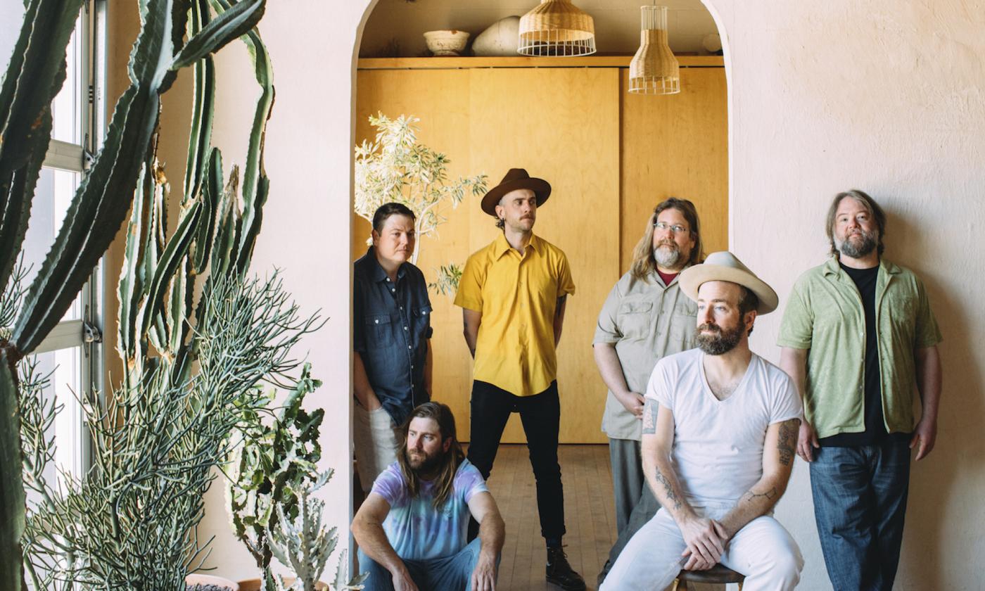 Band members pose in an arched doorway next to a cactus