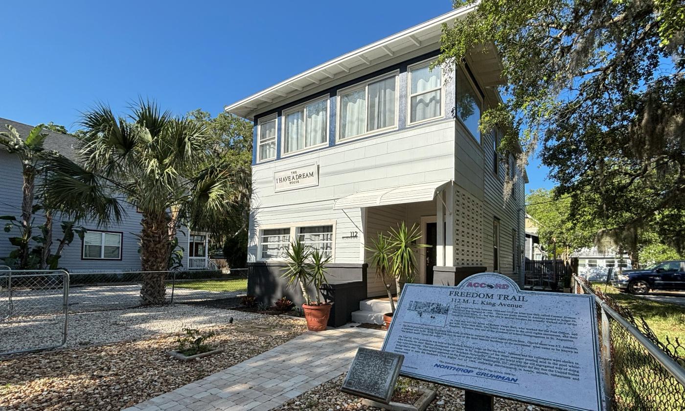 A two story sea foam green slatboard house, ACCORD Freedom Trail marker in the foreground.