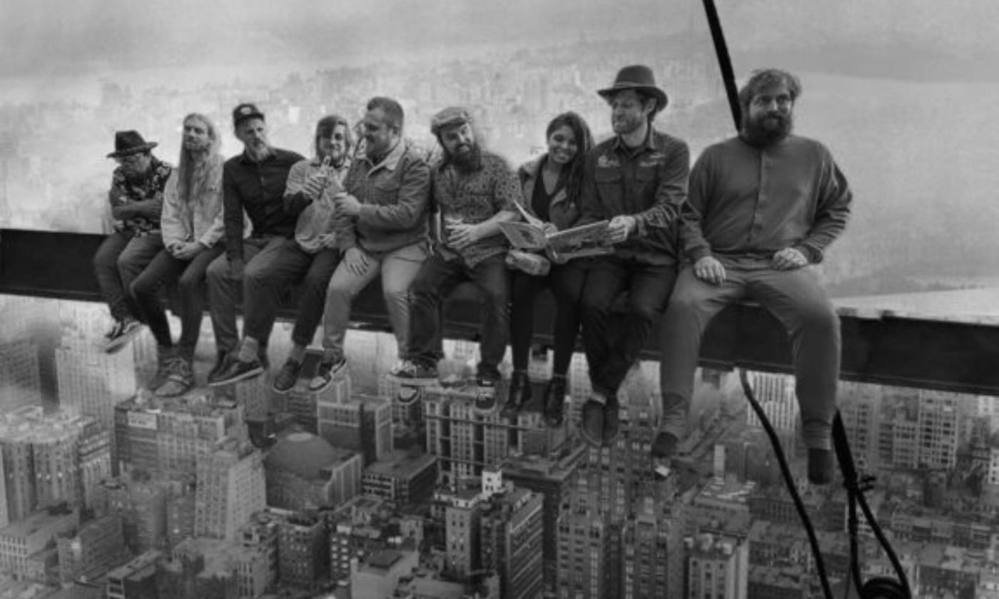 Bandmates from Empire Strikes Brass pose on a long metal beam. 