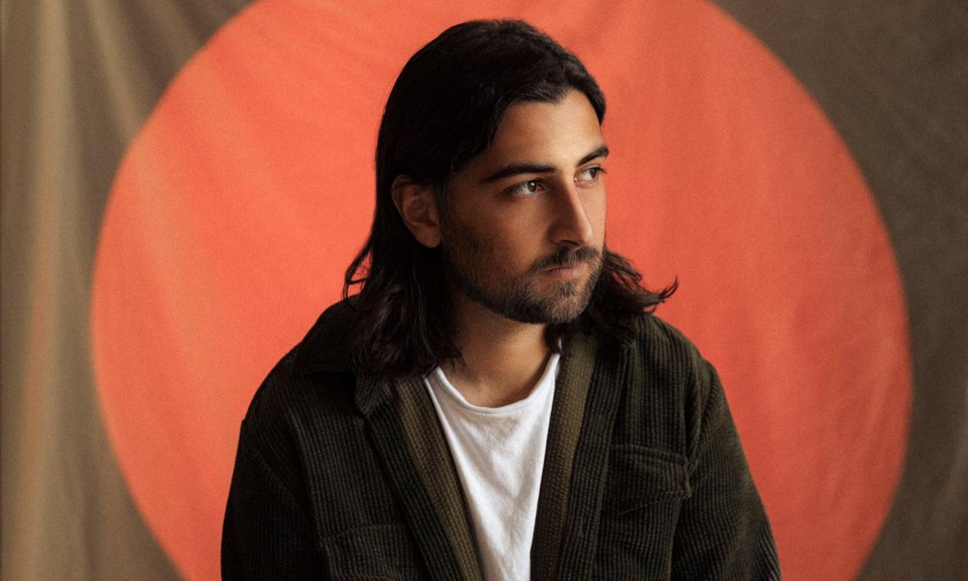 Artist Noah Kahan posing against a minimalist backdrop, framed by a red circle spotlight