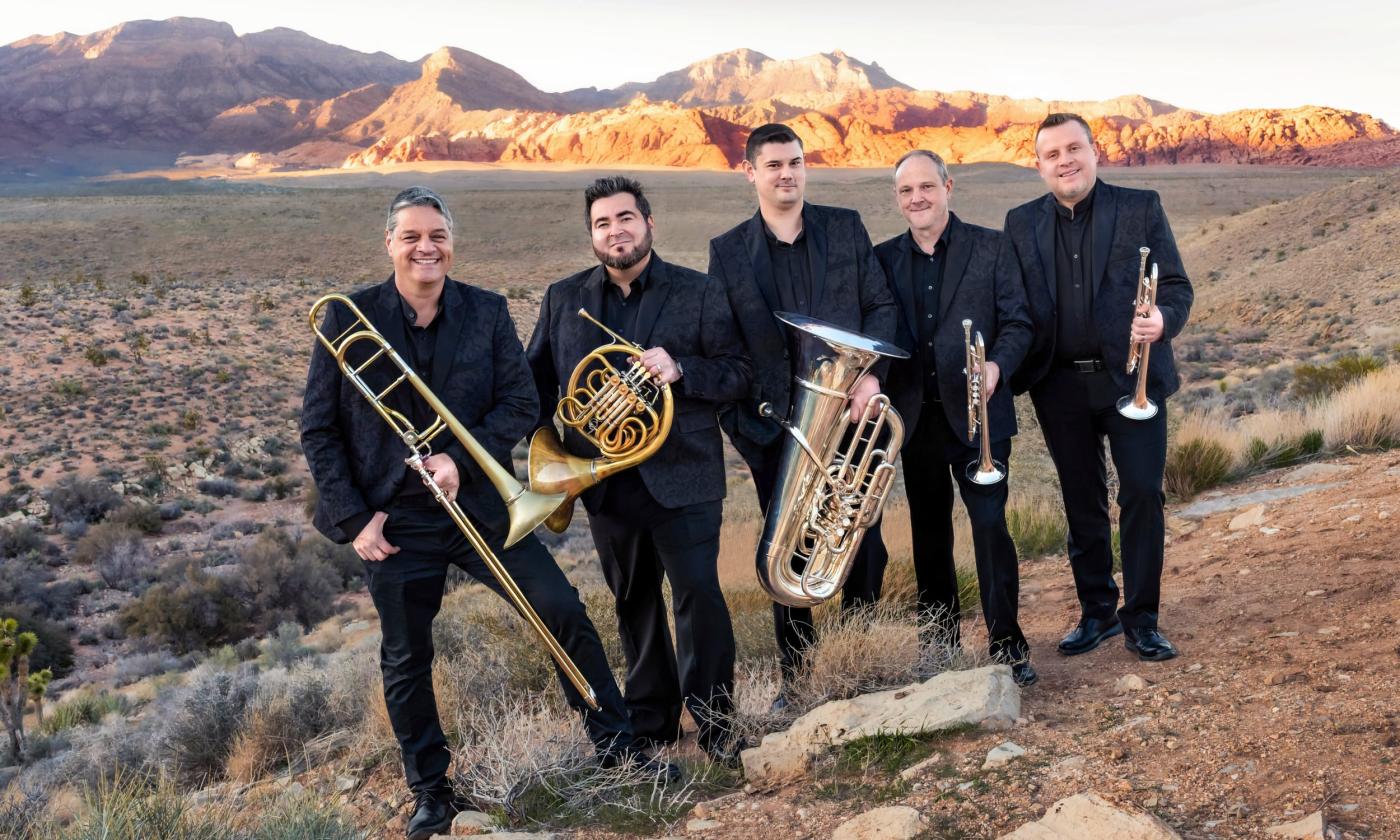 The five members of Boston Brass, wearing black, and standing with their instruments in the desert