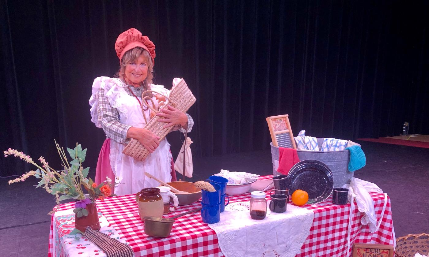 A woman in 19th-century clothing standing at a table depicting her kitchen in a Florida Cracker House