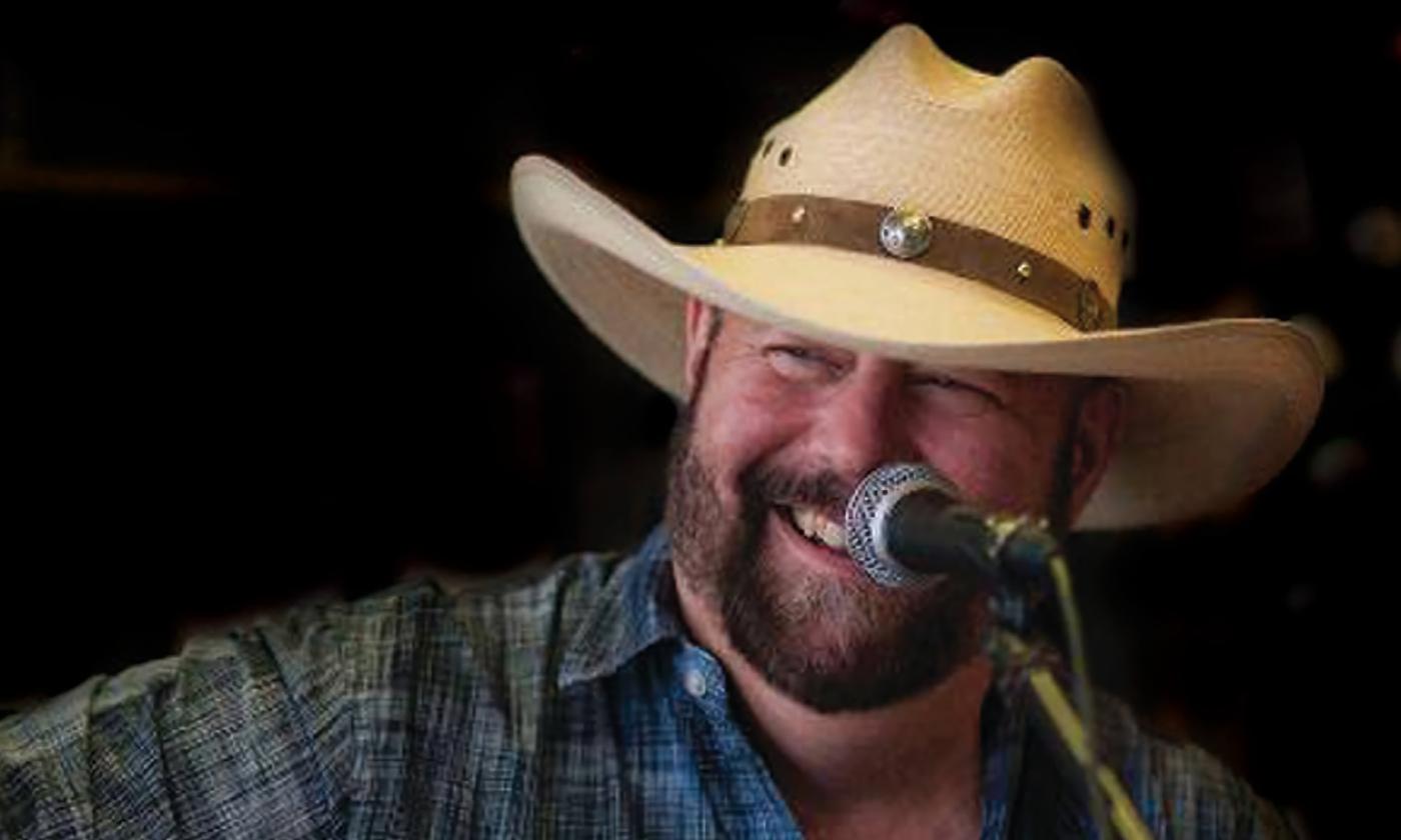 The musician Fond Kiser, in plaid shirt and tan hat, at a microphone