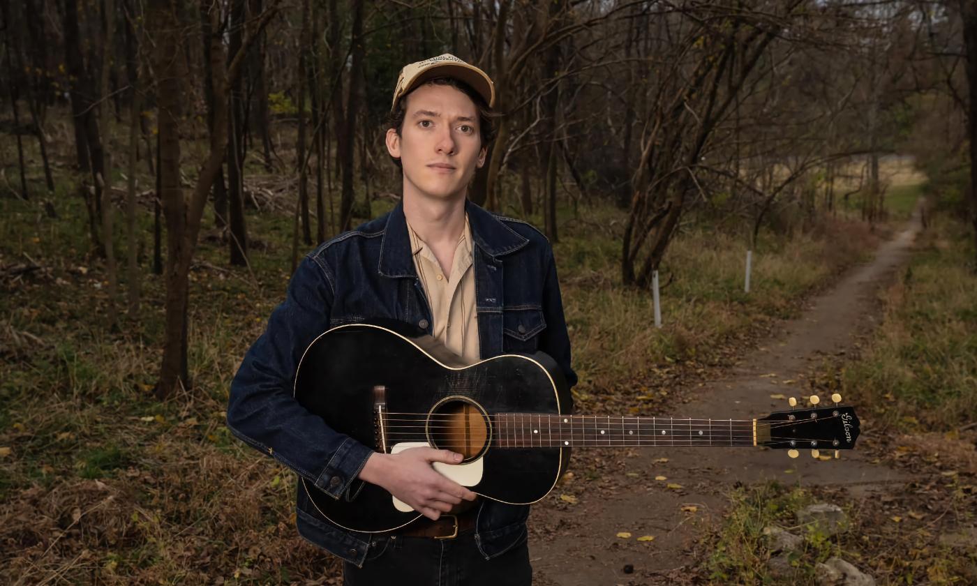 Musician Mason Via in the woods, on a dirt lane with his guitar, in a photo by Michael Weintrob