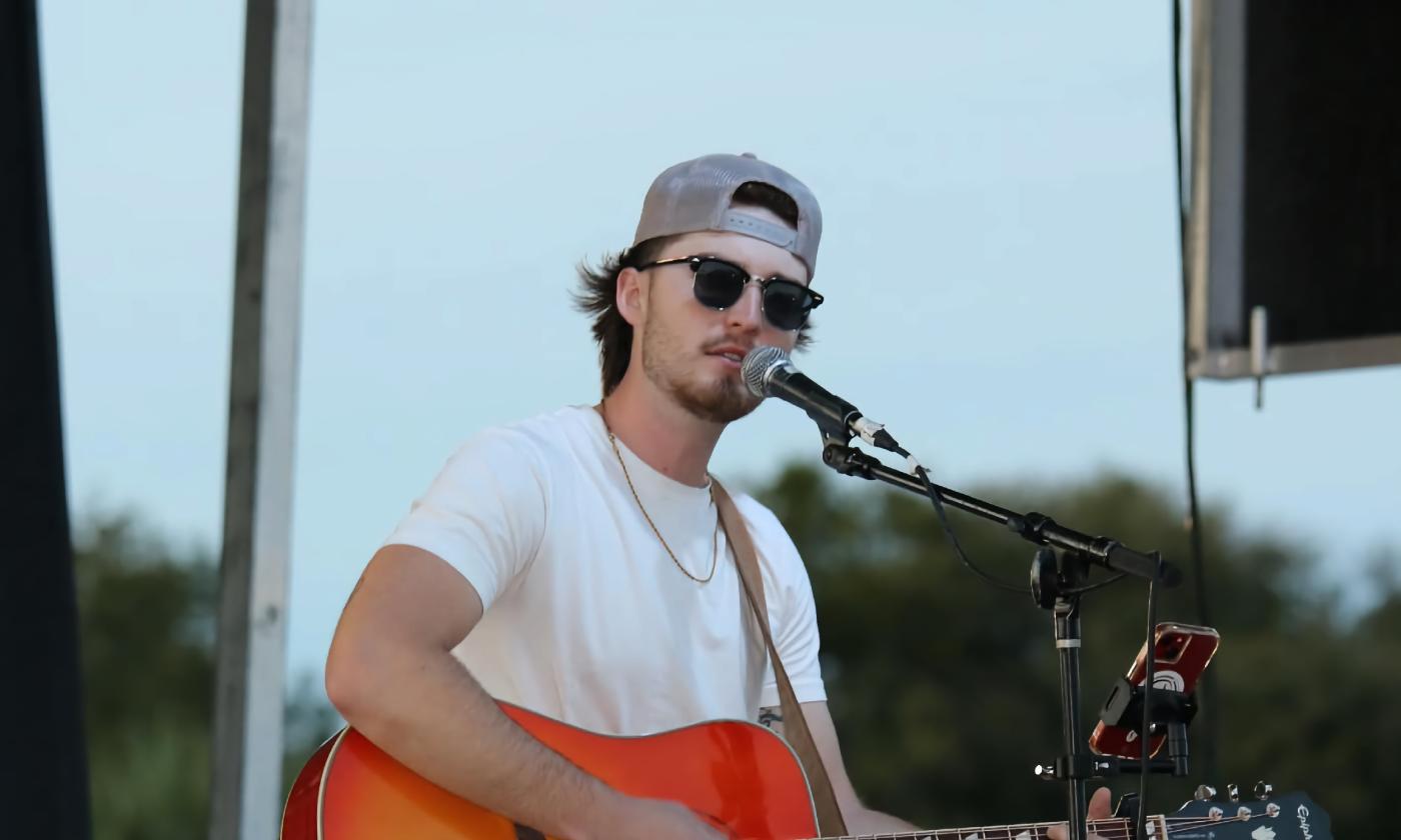 Reece, singing on an outdoor stage, with his guitar