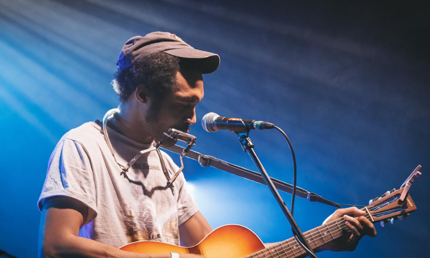 Singer/songwriter Tre' Burt, on stage, in a gimme cap and t-shirt, performing with his guitar