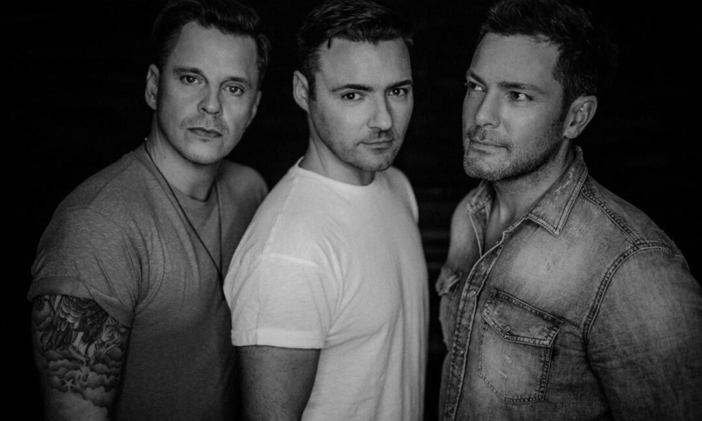 Bandmates from BBMAK pose in a black and white photo with a black backdrop.