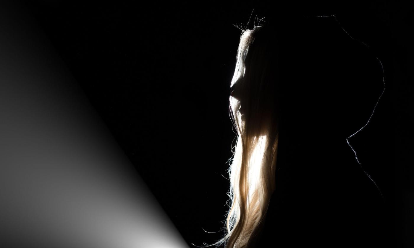 Silhouette of a person, looking at an unseen area illuminated by a flashlight