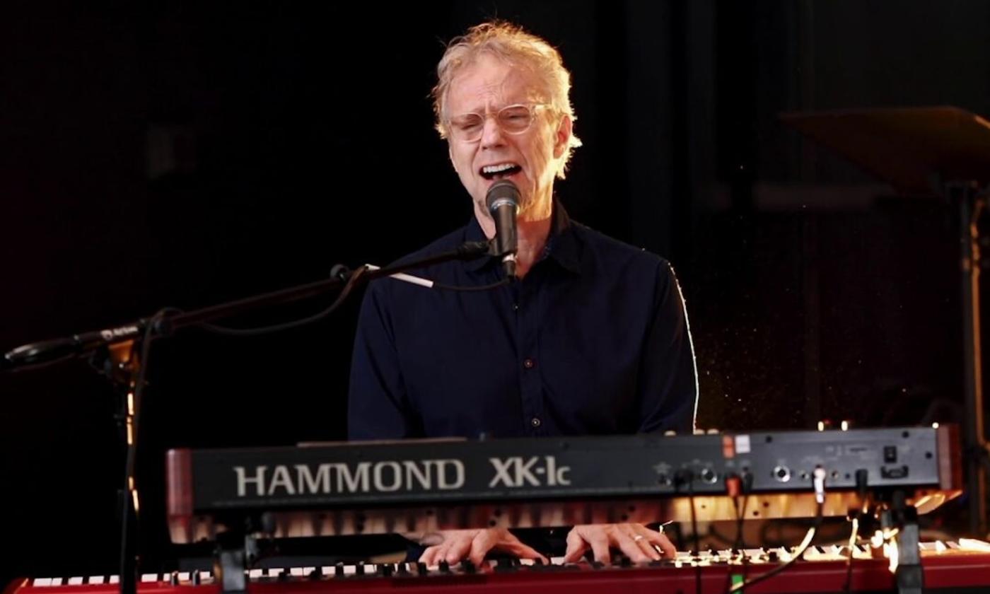 Randall Bramblett sings and plays the keyboard for fans in front of a black backdrop. 