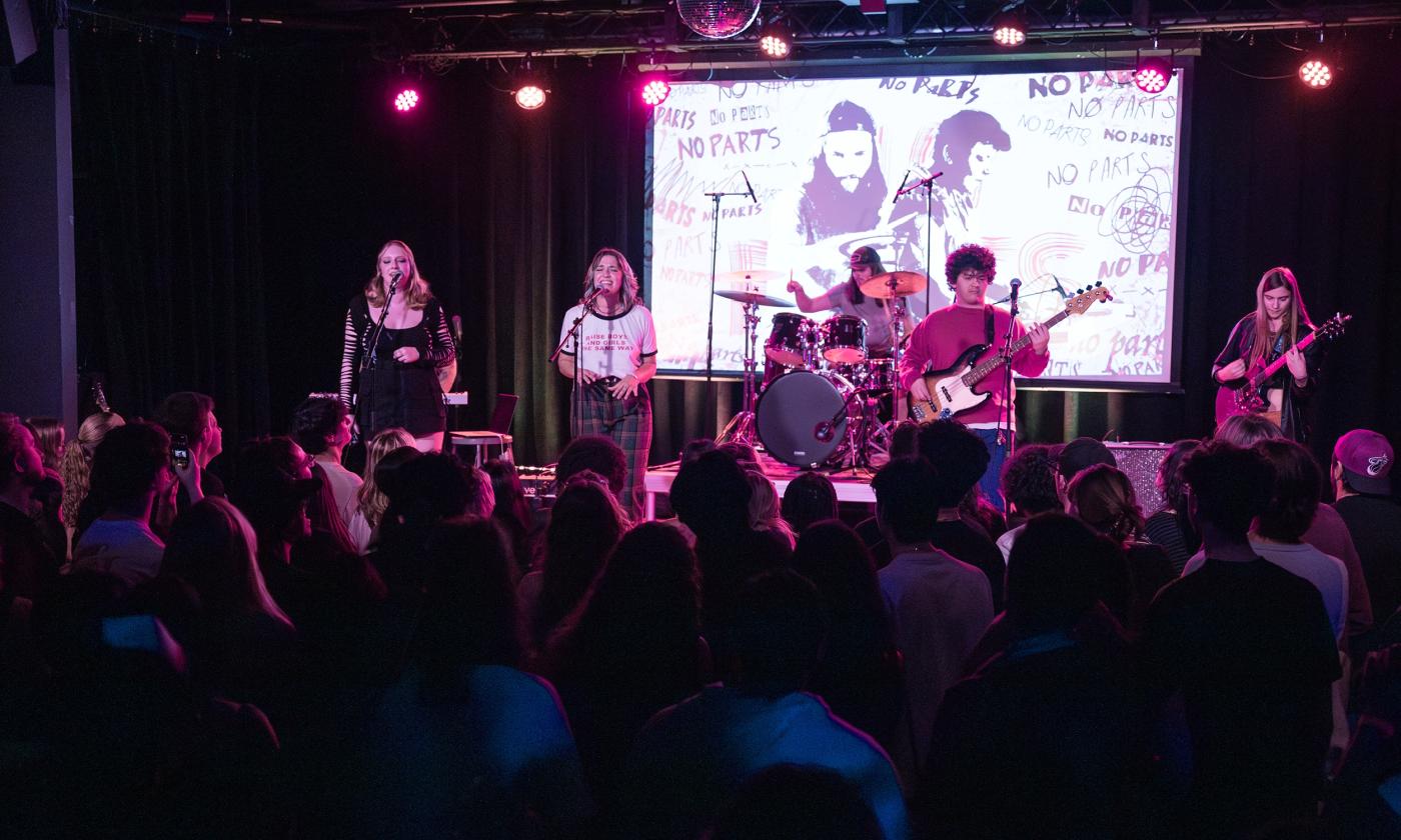 The seven members of No Parts on stage in front of a painted white screen