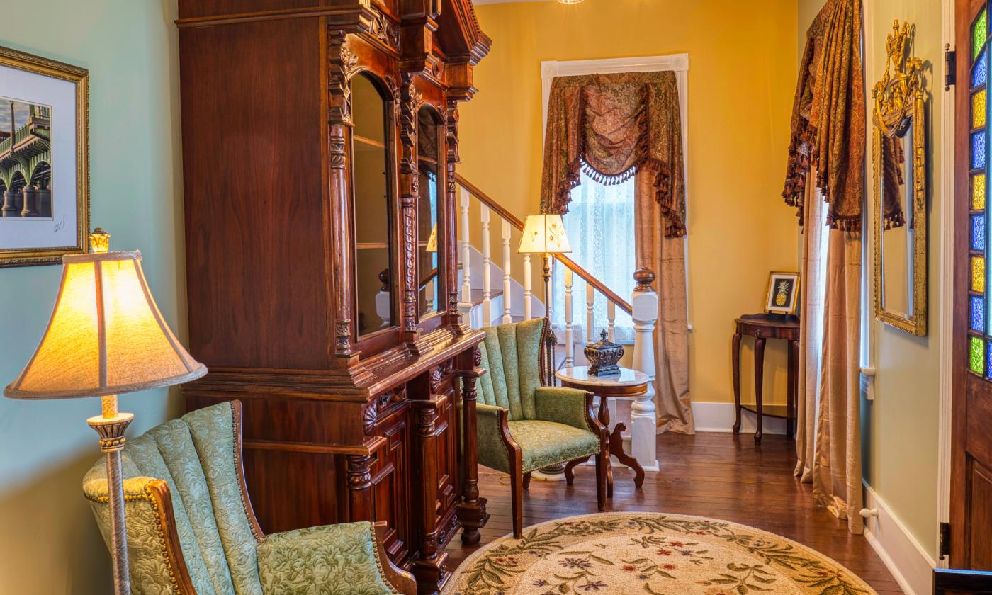 Inside this bed and breakfast, the green and gold-walled entry has stately furniture, area rugs, and a stairway to the second floor