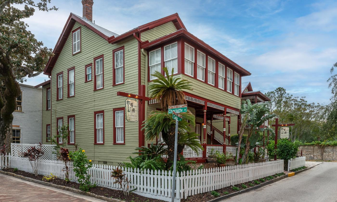 The stately Victorian House Bed n Breakfast, in green with dark red trim surrounded by a white picket fence