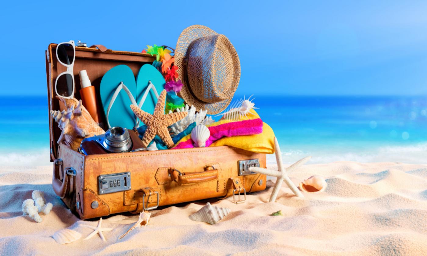 A suitcase full of beach items on the sand next to the ocean