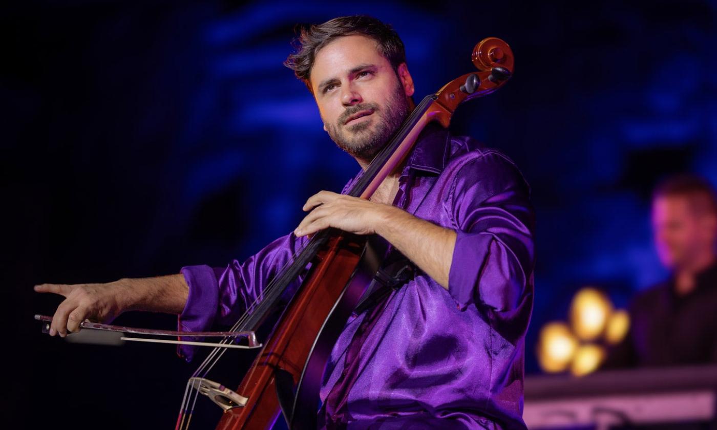 Hauser wears a purple shirt while performing in front of a black and dark blue backdrop.