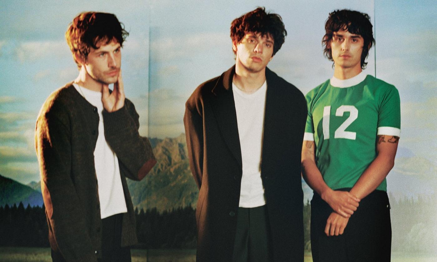 The members of Wallows pose in front of a backdrop designed to resemble a scenic landscape.