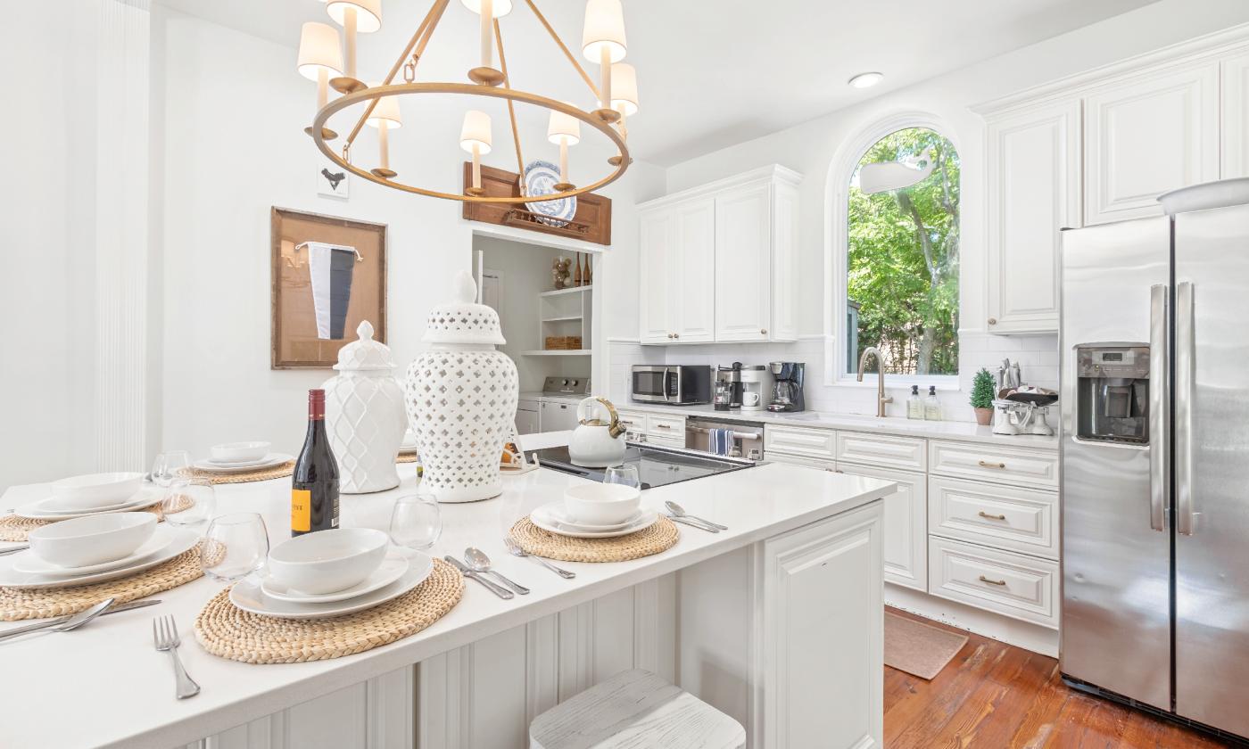 This kitchen in a vacation rental has a white decor, wood floors and a chandelier over the island