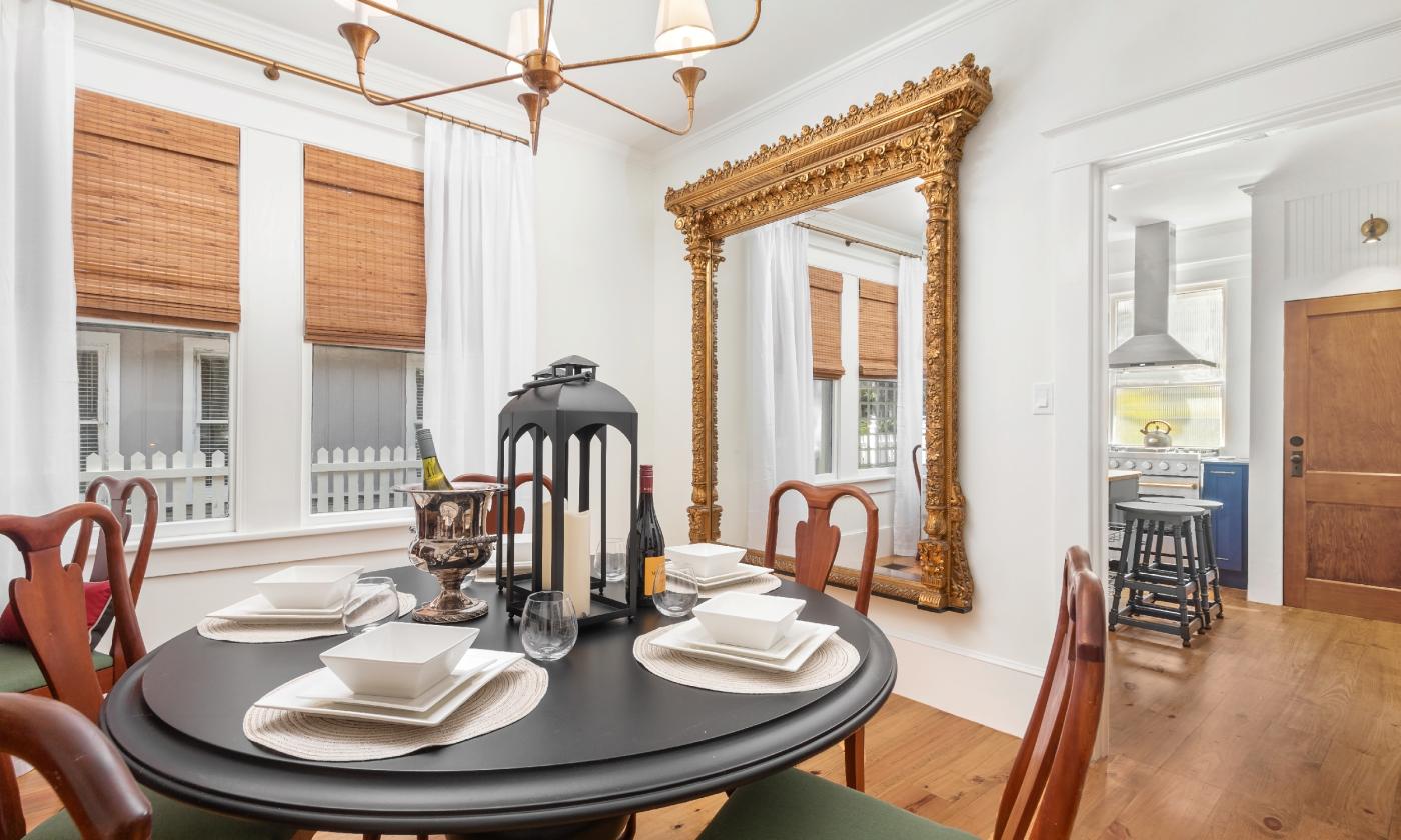 A dining room with a black table, wooden chairs and floor, and large ornate mirror