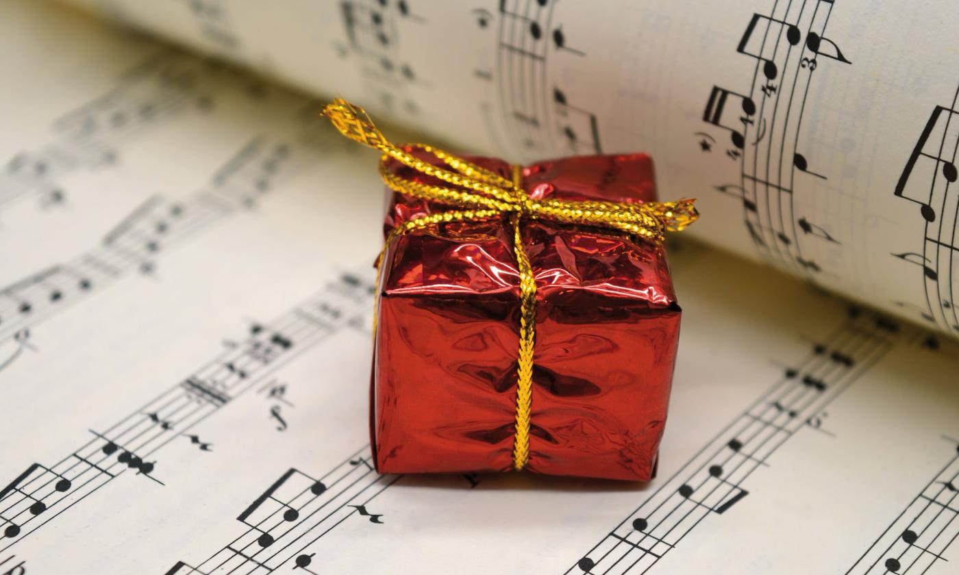 A tiny package, wrapped in shiny red paper with a gold string bow sits on an open sheet of music