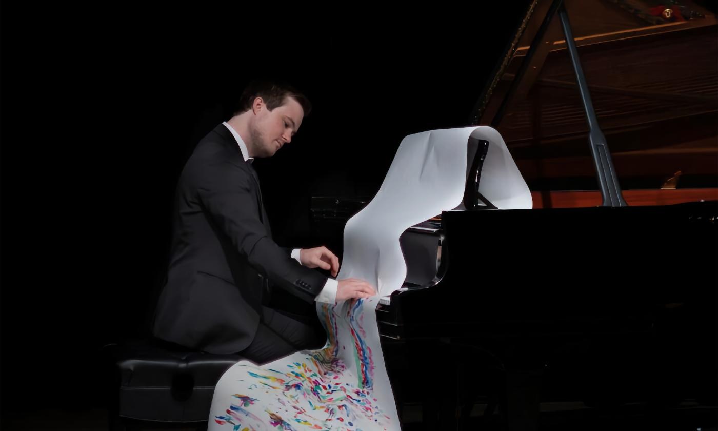 Jazz pianist and composer, Aaron Lehrian, at a piano with a colorful scroll of music