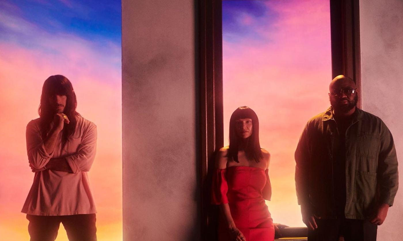 Bandmates from Khruangbin pose in front of a multicolored backdrop. 