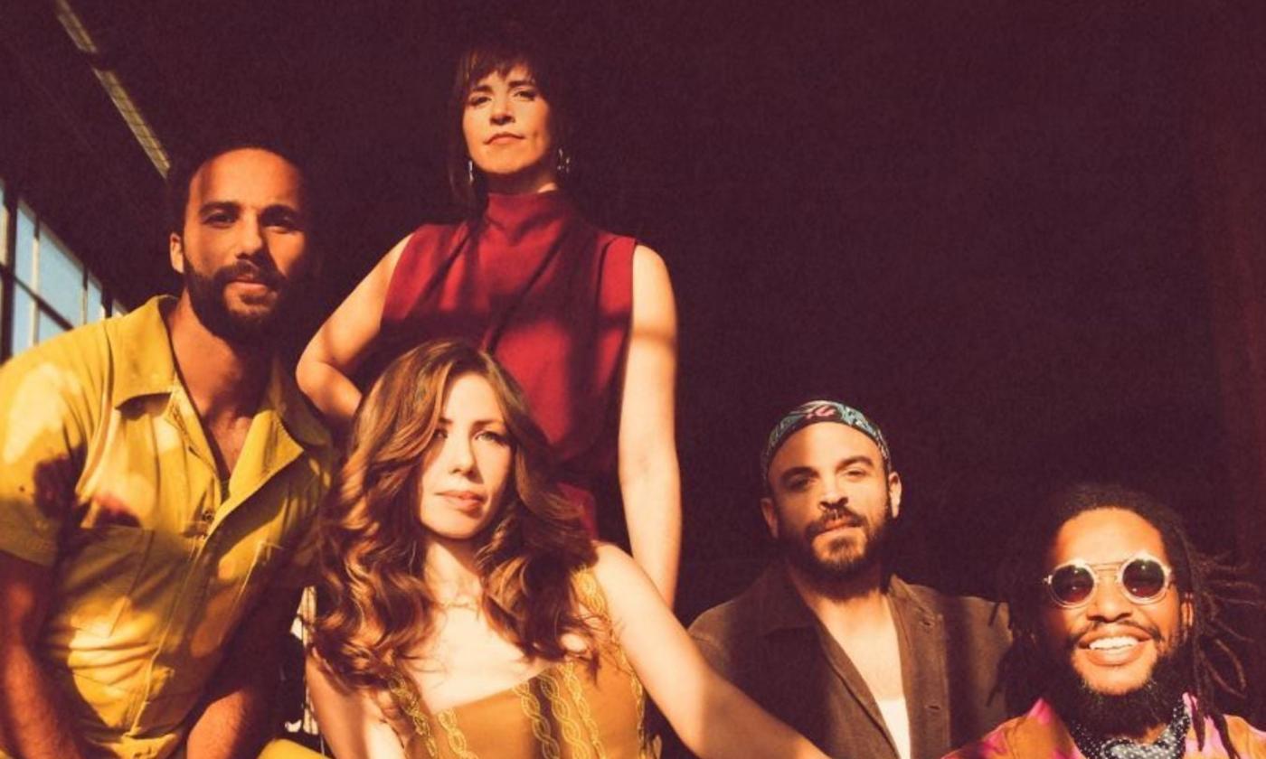 Bandmates from Lake Street Dive pose in front of a black backdrop with a window.