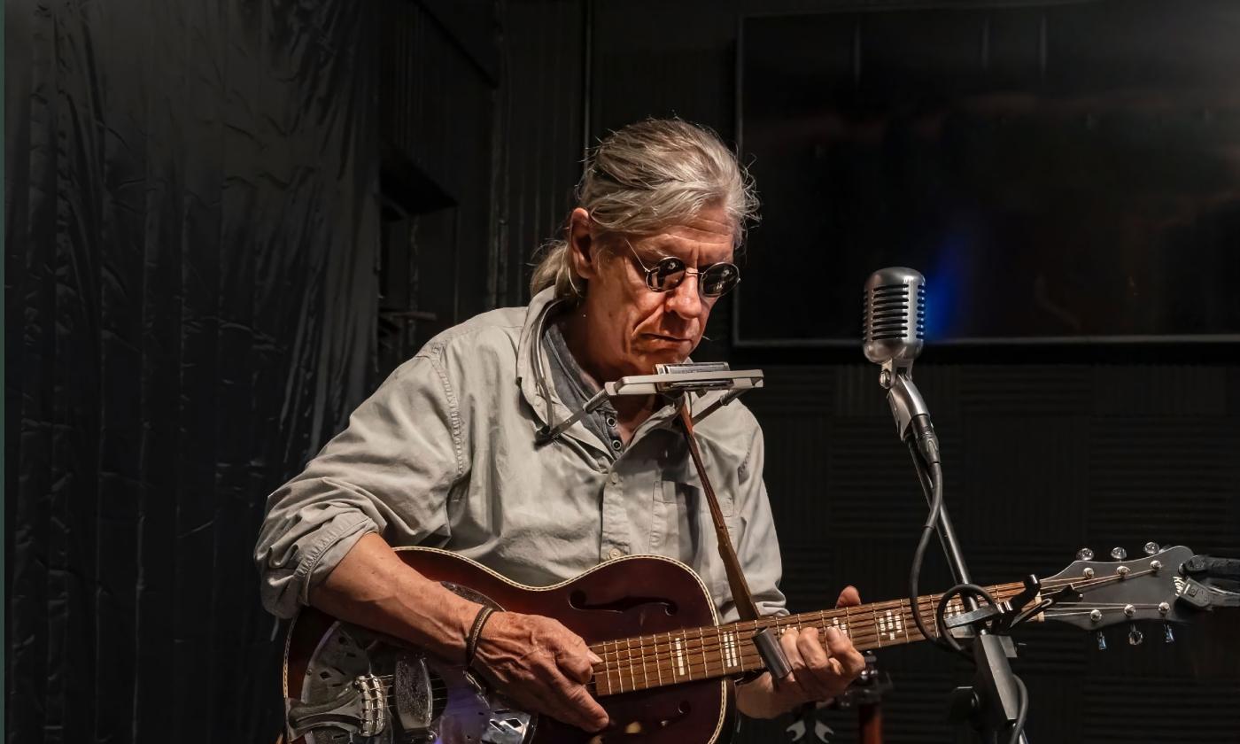 Singer and songwriter Denny Blue performing with guitar and harmonica. Courtesy of Terry Bottom