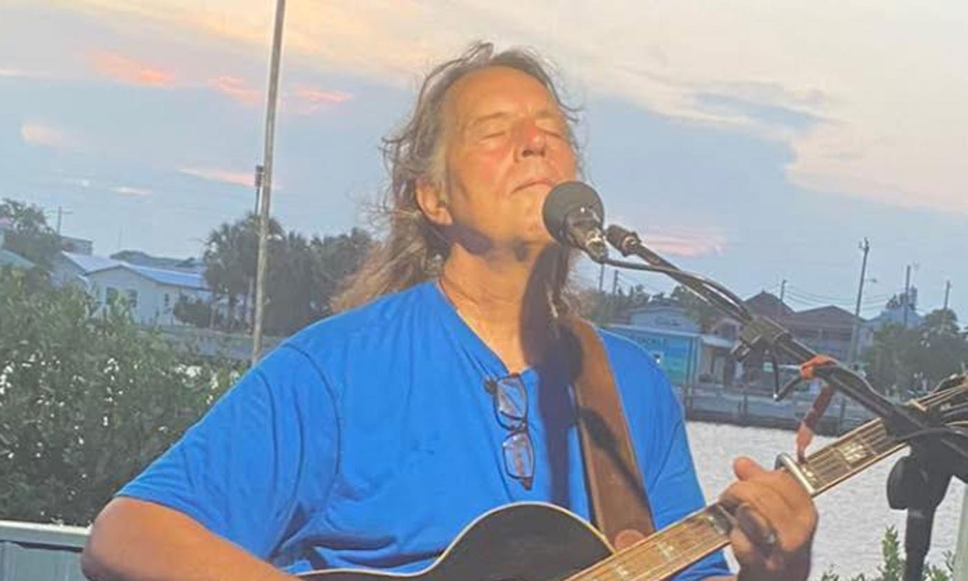 Musician David Wat Besley playing his guitar by the water