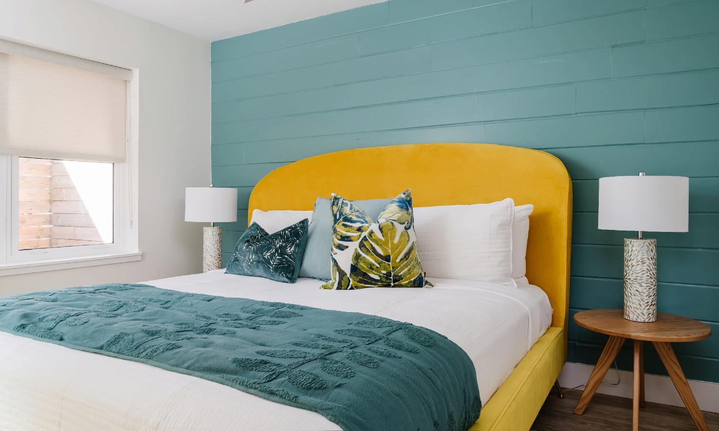 This motel bedroom has a board feature wall painted in teal and a sunny gold bedframe