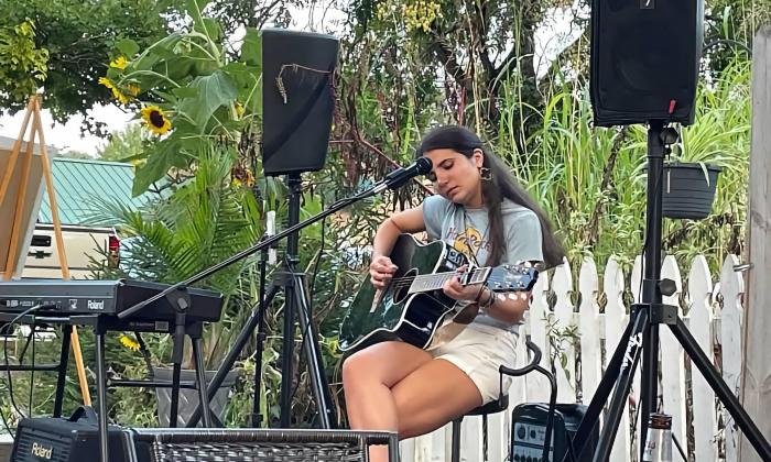 Colleen McKenna playing her guitar on an outside patio stage. 