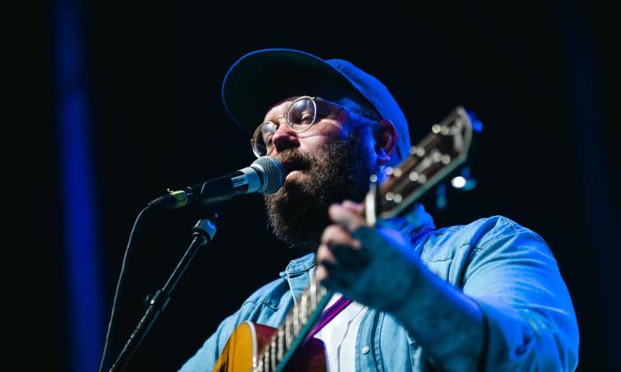 Country singer Josh Hedley performing on stage in front of a microphone with his guitar. 