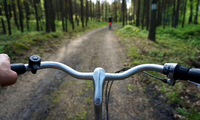 A man holds onto the handles of his bike and steers on a dirt road. 