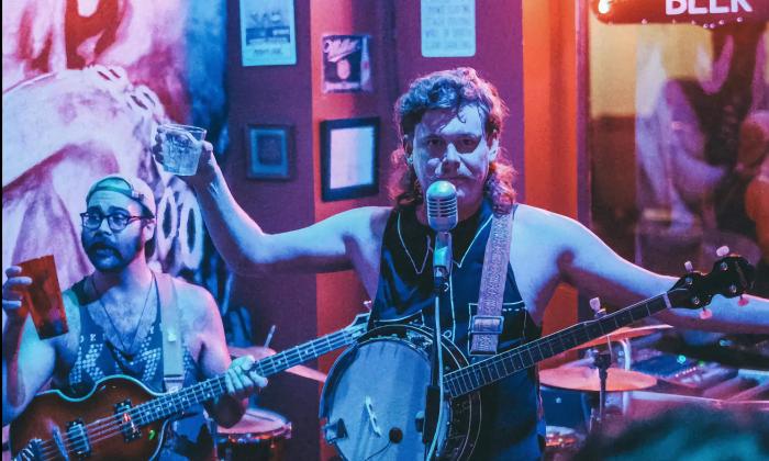 Candid shot of two members of Glizzy Gillespie on a colorful stage, holding their drinks in one hand and their instruments in the other.