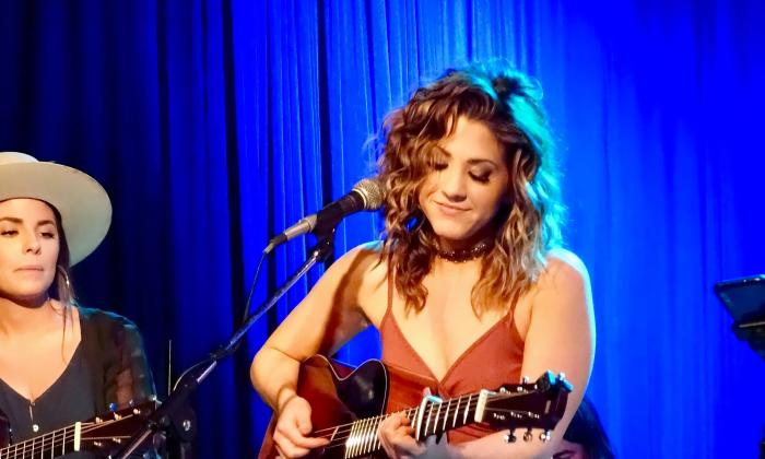 Jamie Floyd at the microphone in the foreground, with her guitar against a blue background