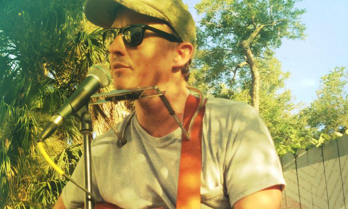 Jeremy Rogers playing guitar and harmonica while singing bluegrass Americana folk