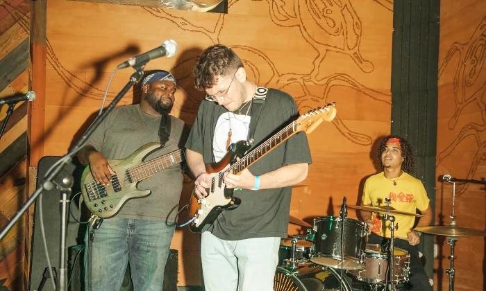 Josh Gluck & The Family Tree performing in a garage-band-style stage with painted plywood walls