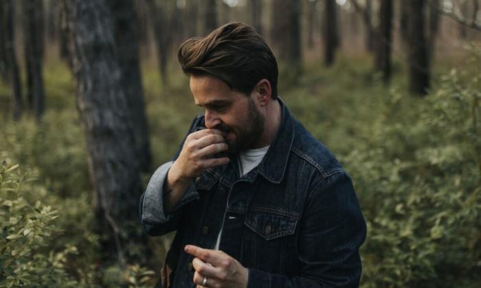 Seth Glier wears dark clothing and poses in the forest. 