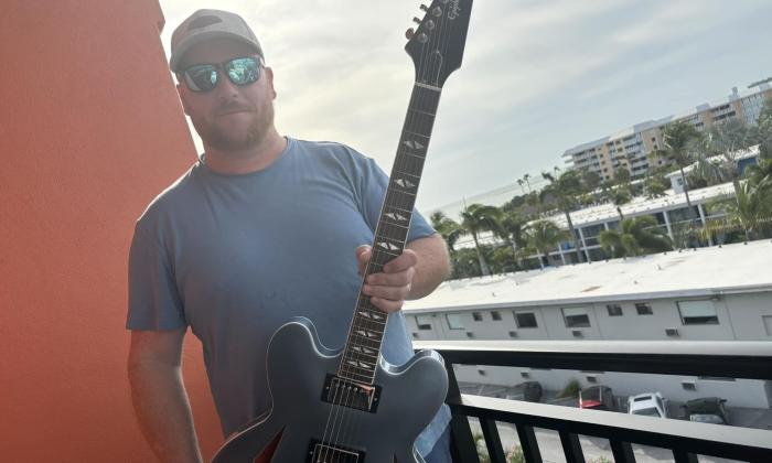 Scott Halls poses with his guitar on a balcony. 