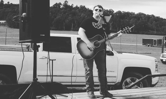 Lane Maury playing his guitar in front of a pick up truck