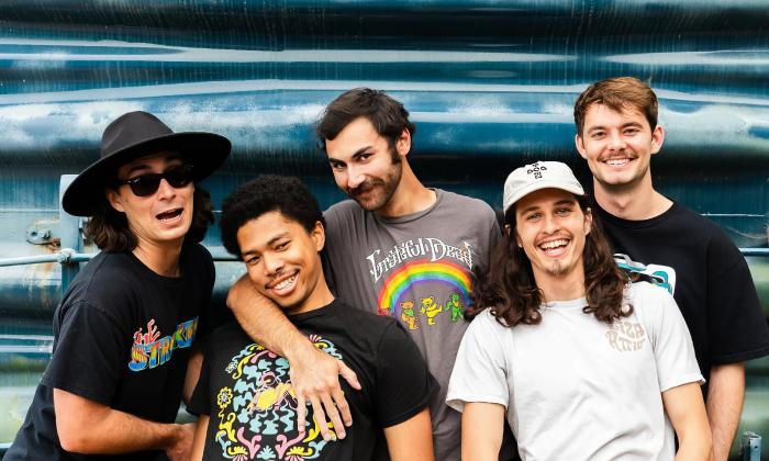 The five-member band, Liza Attic standing against a metal wall