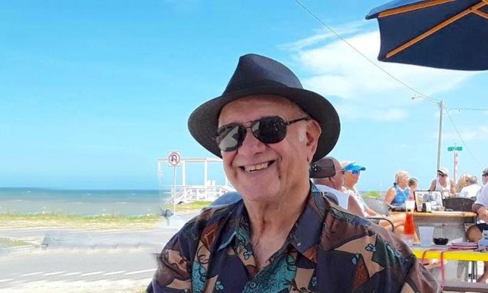 Musician Al Canali at the beach, smiling, in a black hat and sunglasses.