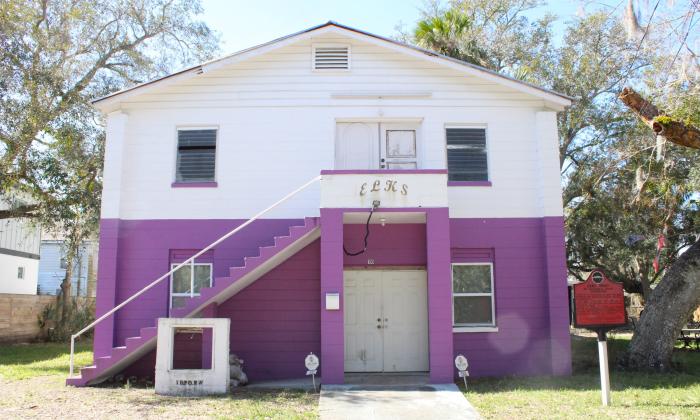 A two story cement block building. Ground floor is painted bright purple, second story painted white. "ELKS" in all caps above the entrance.