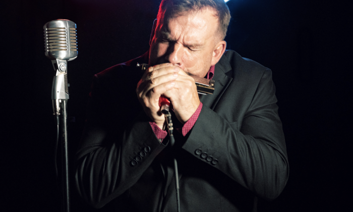 Chris O'Leary shuts his eyes while playing the harmonica on stage. 